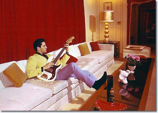Elvis Presley wearing cool colour combinations - sitting on sofa playing his guitar