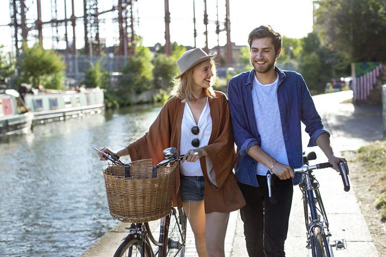 couple-smiling-and-walking-along-canal-with-bikes-